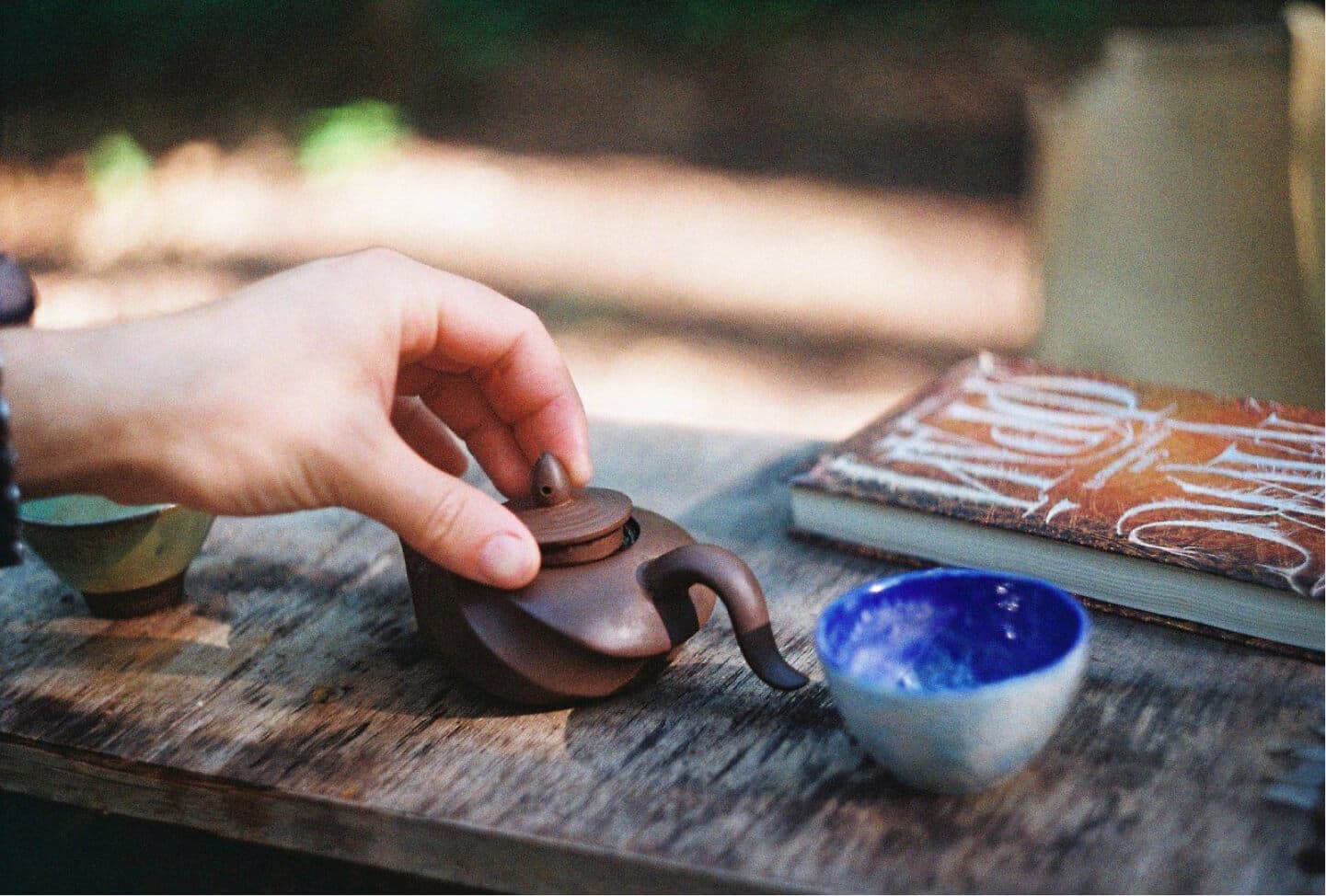 A hand placing a lid on a small teapot on a rustic wooden surface